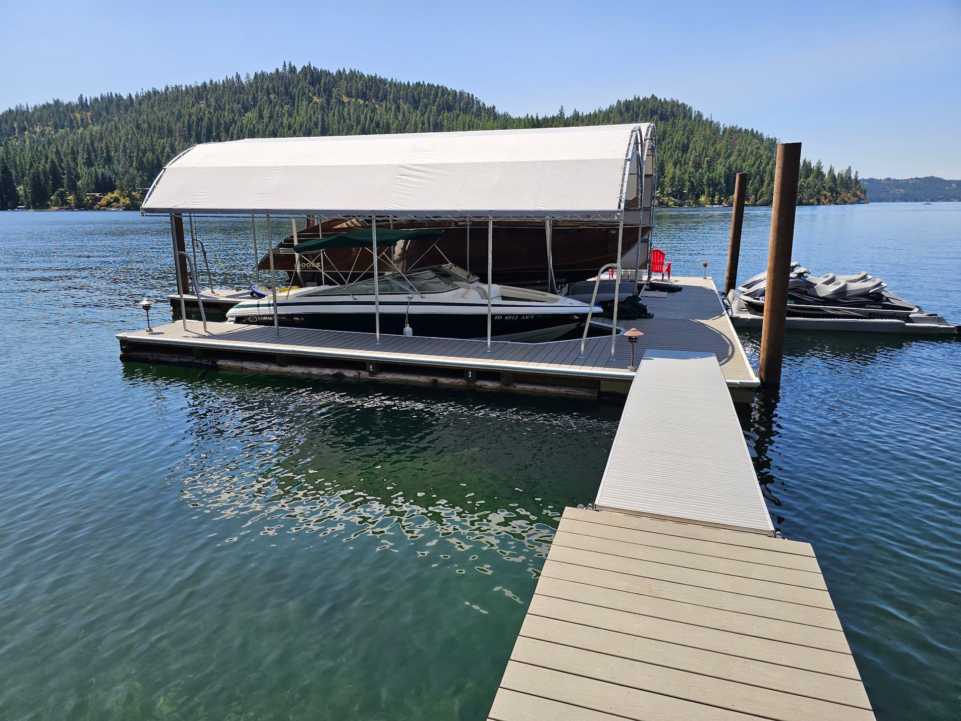 A custom cedar-log floating dock with boat lift, canopy and composite decking, built by Jake On The Lakes on a North Idaho lake